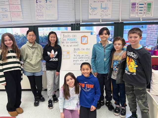 Group of happy 4th grade students posing for a picture next to a poster in the classroom