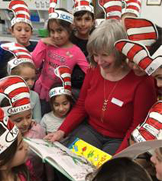 Students dressed up as the cat in the hat surround a teacher reading Dr. Seuss