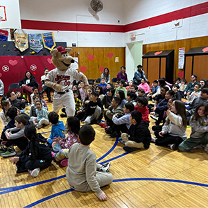 Jack the Jackal running by students sitting on the gym floor