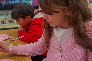 Two students writing on pink paper hearts