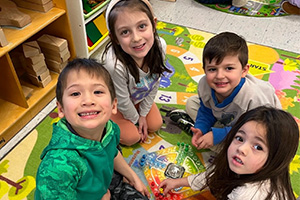 Four students sitting around a game and smiling at the camera