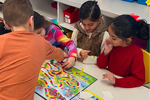 four students sitting at a table playing a board game