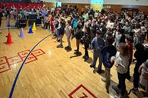 A crowd of students in the gym in front of cubes taped on the floor with numbers in them