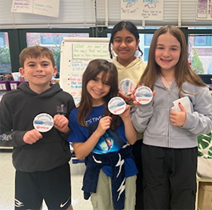 Four 4th graders holding large round Veolia buttons